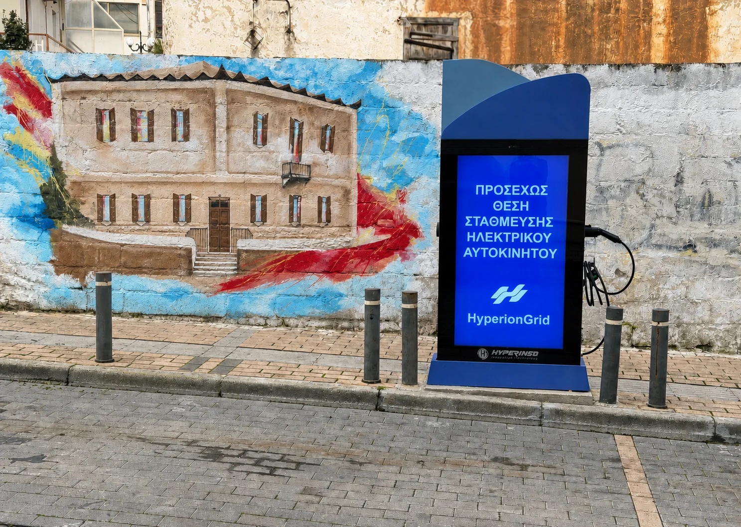 A Hyperinso charging station with a digital screen in the Municipality of Mandra-Eidyllia, in front of a public mural